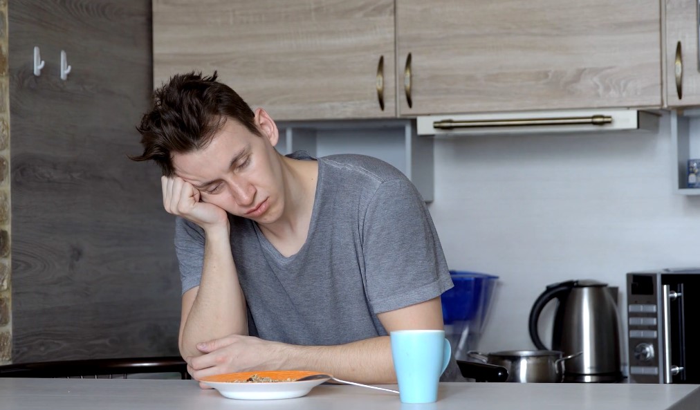 Guy sleeps in a kitchen while seating in a chair
